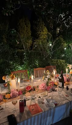 an outdoor dinner table is set with candles and flowers on it, surrounded by greenery