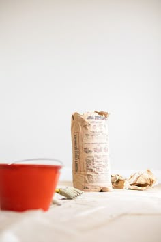 a red bowl sitting on top of a white bed next to a bag of food