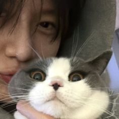 a woman holding a gray and white cat in her arms while looking at the camera