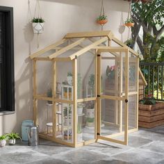 a small wooden greenhouse sitting on top of a cement floor next to potted plants