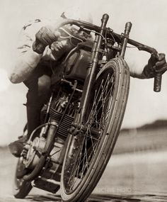 an old black and white photo of a man on a motorcycle with a sack strapped to the front wheel