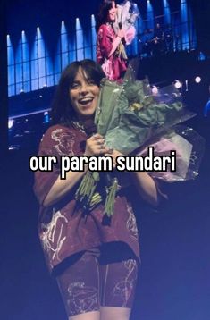 a woman is holding flowers and smiling while standing in front of a stage with the words our param sundari