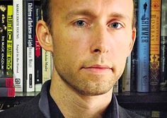 a man standing in front of a bookshelf with many books on the shelves