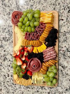 a wooden platter filled with grapes, strawberries, cheeses and meats