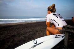 a woman sitting on top of a beach next to a surfboard in front of the ocean