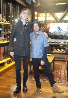 two young men standing next to each other in a room with wooden floors and furniture