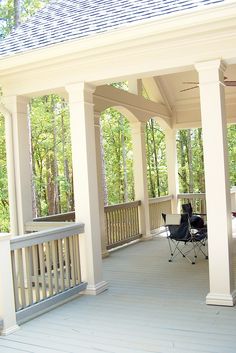 an outdoor covered porch with chairs and table on the front deck, surrounded by trees