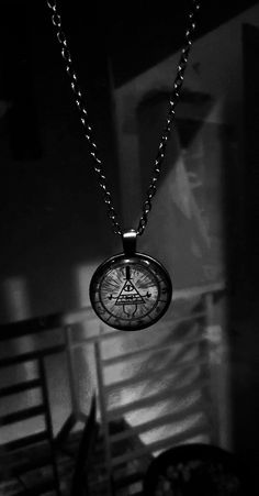 a black and white photo of a compass pendant on a chain with a chair in the background