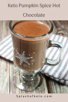 a glass mug filled with hot chocolate on top of a wooden table next to a striped napkin