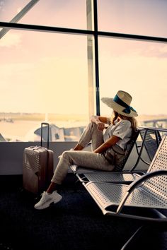 a woman sitting on top of an airport bench next to a luggage bag and suitcase