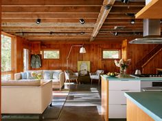 a kitchen and living room with wood paneling on the walls, couches, coffee table and stairs