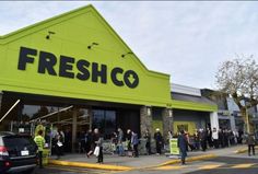 a large group of people standing in front of a fresh co store on a city street