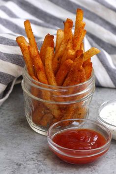 a glass jar filled with french fries next to a small bowl of ketchup