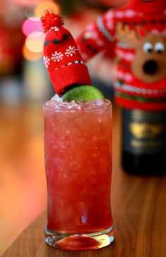 a red drink with a green apple in it on a table next to a teddy bear