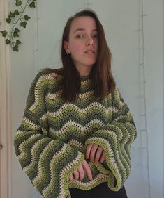 a woman standing in front of a wall wearing a green and white crocheted sweater