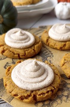 pumpkin cookies with cream cheese frosting on a paper towel next to some pumpkins