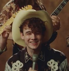 a young man wearing a cowboy hat and holding a microphone