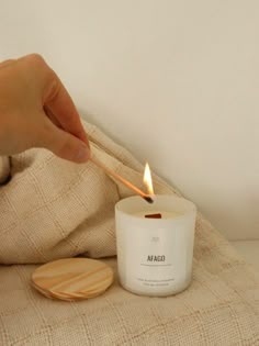 a person lighting a candle on top of a bed next to a wooden coaster and blanket