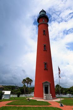 a red light house sitting on top of a lush green field under a blue cloudy sky