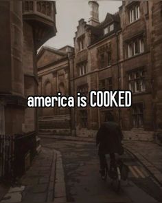 a man riding a bike down a street next to tall buildings with the words america is cooked