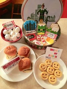 two plates with hamburgers and mini sandwiches on them, next to a tin lunch box