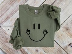 Stay warm and cozy with our Funny Middle Finger Sweatshirt, a perfect blend of comfort and humor! This Funny Smiley Face Sweater adds a playful twist to the classic happy face, making it a great choice for anyone with a fun sense of style. Whether you're lounging at home or out with friends, this Smiling Face Crewneck is perfect for those who love unique humor. Ideal as a Unique Humor T-Shirt for Teens or a Funny Party Happy Face Tee, it's sure to bring smiles and laughs wherever you go!   *Fast shipping in 2-5 Business Days! *Comfy unisex sweatshirts are soft and durable. *Measuring tip: Take your favorite sweatshirt or tee, lay it on a flat surface and measure the width (armpit to armpit) and length (top to bottom), then compare with our size chart. *Classic fit, durable and soft, poly/c Fun Crew Neck T-shirt For Loungewear, Funny Winter Top With Text, Winter Funny Style Top With Text, Winter Funny Text Top, Trendy Funny Print Tops For Winter, Funny Long Sleeve Tops With Text, Funny Winter Streetwear Tops, Fun Winter T-shirt With Crew Neck, Casual Winter Tops With Smiley Face