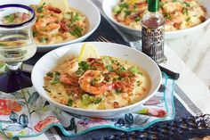 three bowls filled with shrimp and grits on top of a table next to wine glasses