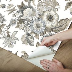 a woman is cutting paper on top of a table with flowers and leaves printed on it