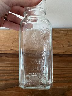 a hand is holding a glass jar with some writing on the bottom and inside it