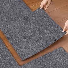 two hands are placing carpet on the floor