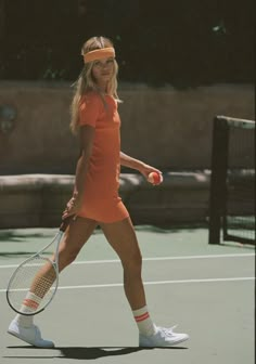 a woman holding a tennis racquet on top of a tennis court in an orange dress