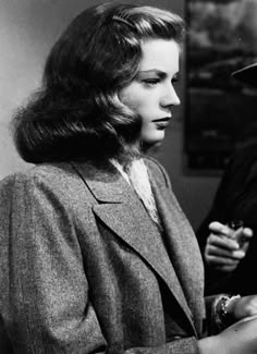 an old black and white photo of a woman in a hat looking at her cell phone