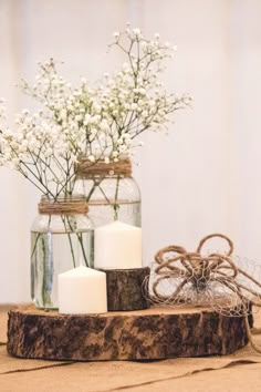 some white flowers are in a glass jar on a wooden stand with rope and twine