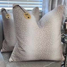 two pillows with tags on them sitting next to each other in front of a window