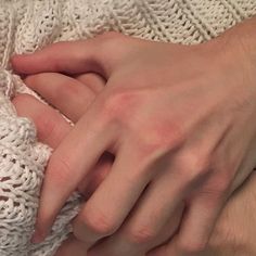 a close up of a person's hand on top of a white knitted blanket