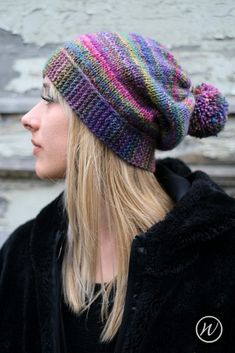 a woman with blonde hair wearing a multicolored knitted hat and black jacket