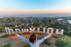 a woman standing on top of a hill with her arms wide open in front of the hollywood sign