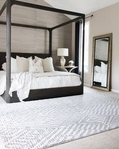 a bedroom with a four poster bed and white linens on the floor, along with a large mirror