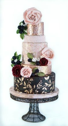 a three tiered cake with roses on top is decorated in gold, black and pink