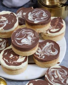 there are many cookies with chocolate frosting on the white plate next to gold spoons