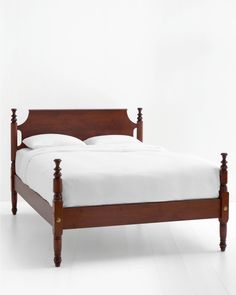 a wooden bed frame with white sheets and pillows on it's headboard, in front of a plain white wall