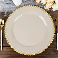 a white plate with gold trim on it next to silverware, flowers and napkins