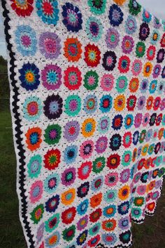 a crocheted granny's afghan hanging on a clothes line in the grass