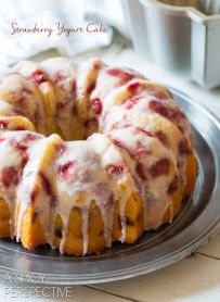 a strawberry yogurt cake with icing on a metal plate next to a cup