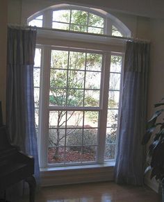 a living room with a piano in the corner and a window that has curtains on it