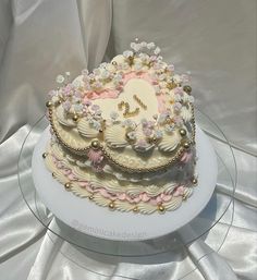 a three tiered cake decorated with flowers and pearls on a clear platter sitting on a white table cloth