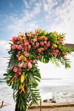 a floral arch with pink flowers and green leaves on the ocean shore near the beach