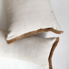 two white pillows with brown fringes on them