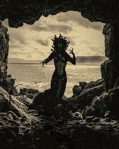 an image of a woman standing in the cave looking out at the water and rocks