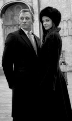 a man and woman standing next to each other in front of a building with an archway